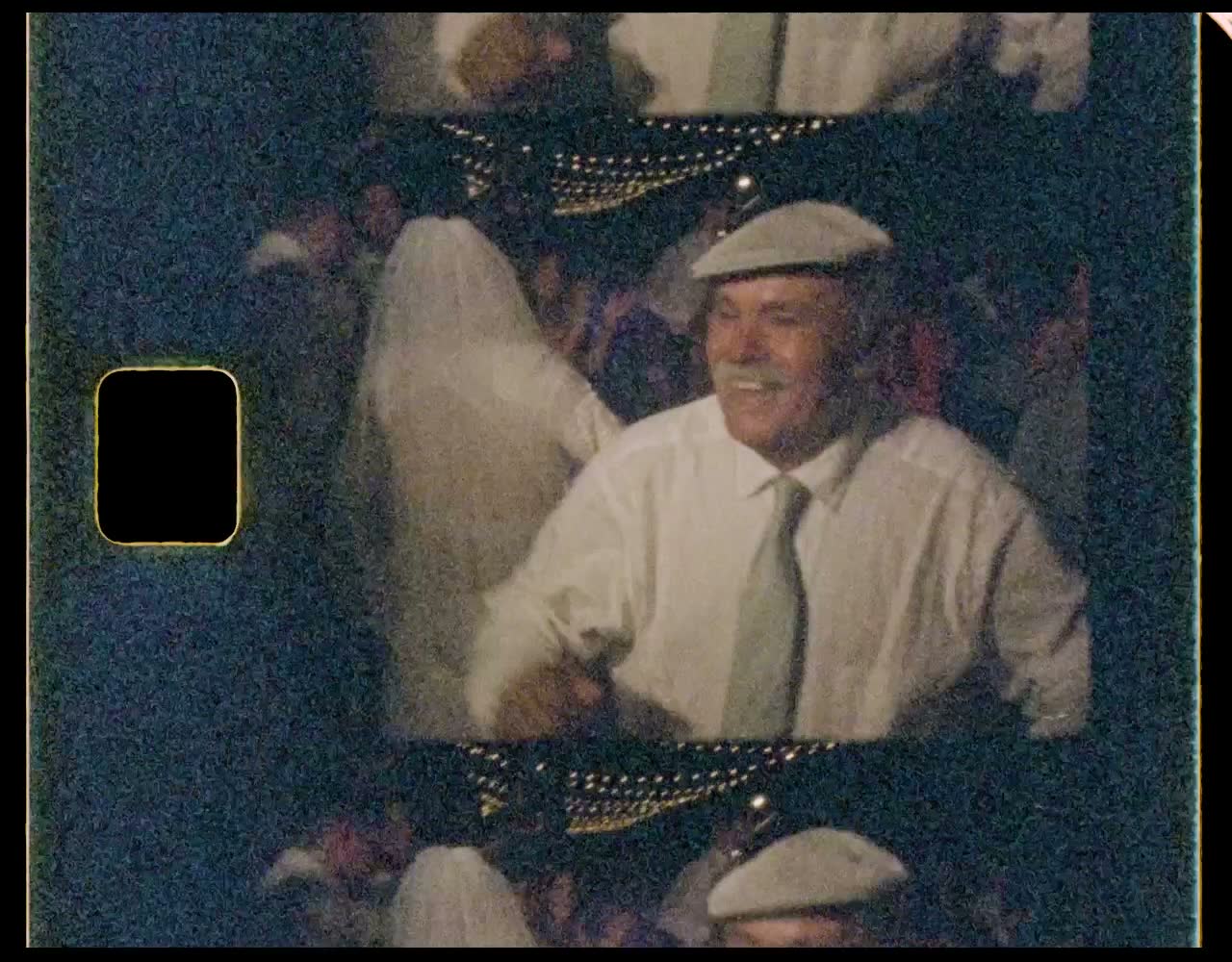 An older man in a flat cap laughing on the dance floor